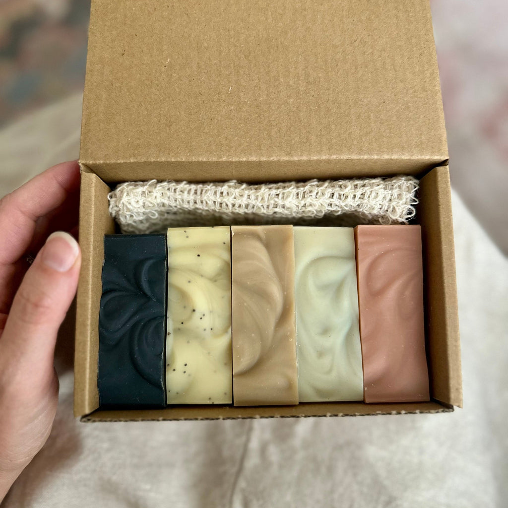 Set of five soaps in a cardboard box held by a hand.