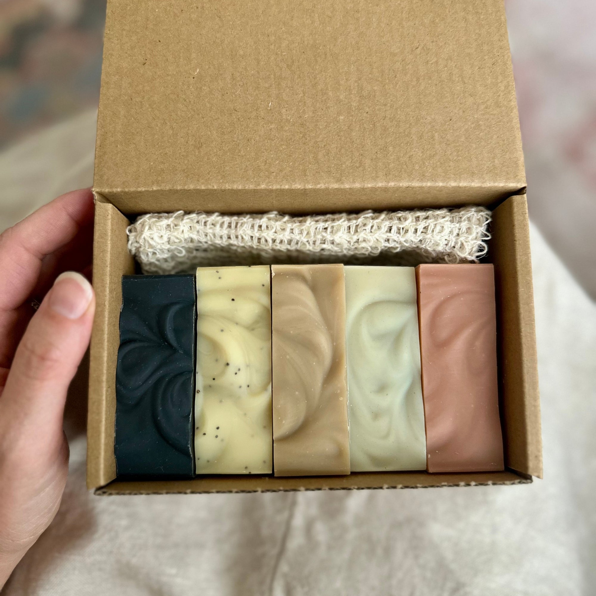 Set of five soaps in a cardboard box held by a hand.