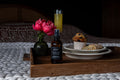 Wooden tray with a bottle of 'Farmhouse Fare' product, a vase with pink flowers, and a plate of pastries on a textured surface.